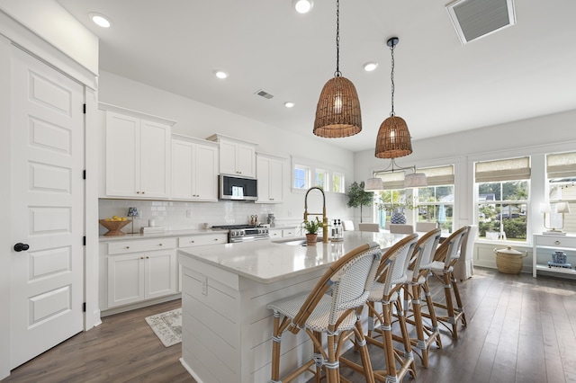 1713 Banning St, Mount Pleasant, SC 29466 - kitchen featuring stainless steel appliances, a center island with sink, dark wood finished floors, decorative backsplash, and white cabinetry