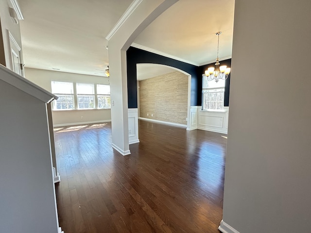 interior space with dark wood-style floors, a wainscoted wall, crown molding, and ceiling fan with notable chandelier