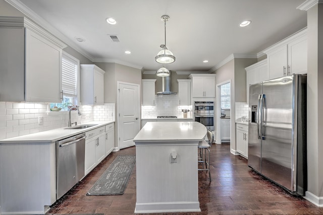 kitchen featuring visible vents, a sink, appliances with stainless steel finishes, wall chimney exhaust hood, and a center island