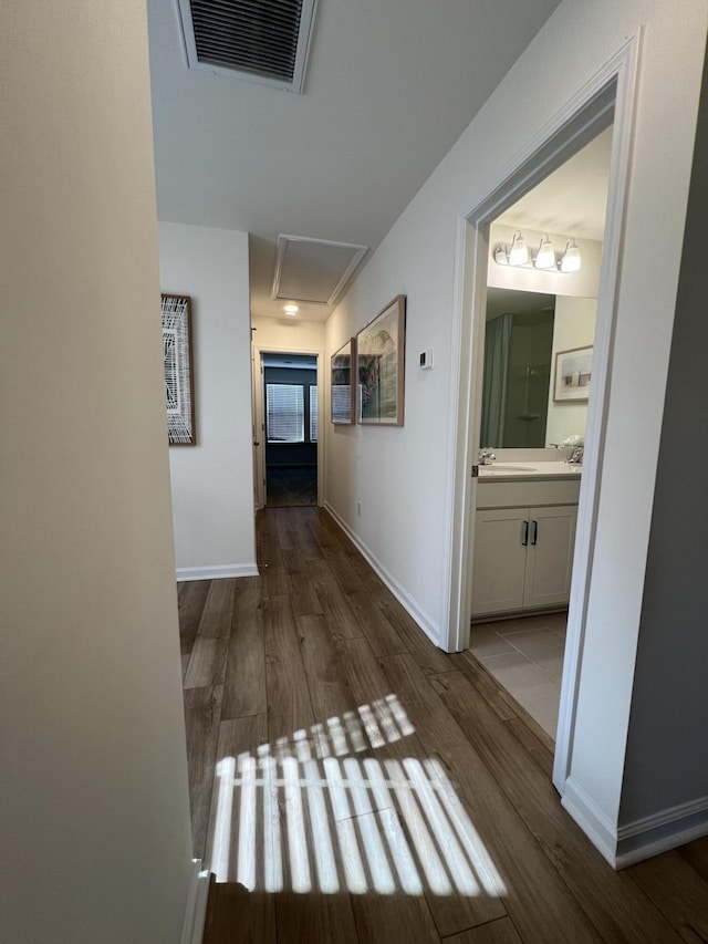 hallway featuring baseboards, visible vents, a sink, and light wood finished floors