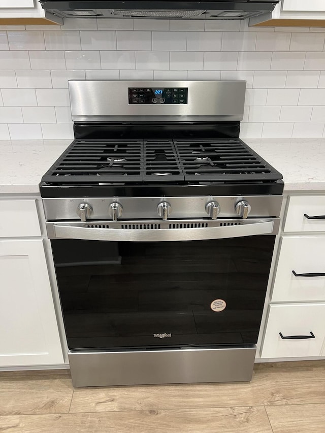 interior details featuring light stone counters, backsplash, white cabinets, gas range, and light wood-type flooring