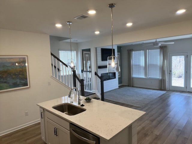 kitchen with a kitchen island with sink, a sink, white cabinets, stainless steel dishwasher, and pendant lighting