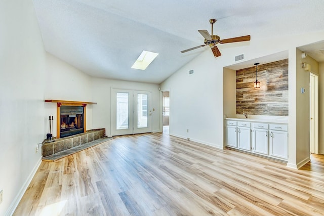 unfurnished living room with vaulted ceiling with skylight, ceiling fan, a tiled fireplace, and light wood finished floors