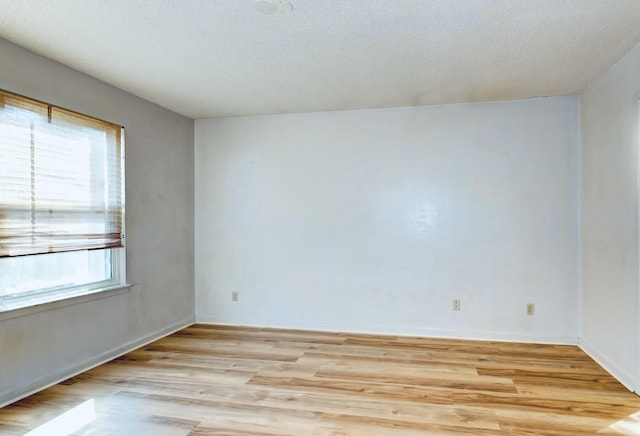 spare room with a textured ceiling, light wood-type flooring, and baseboards