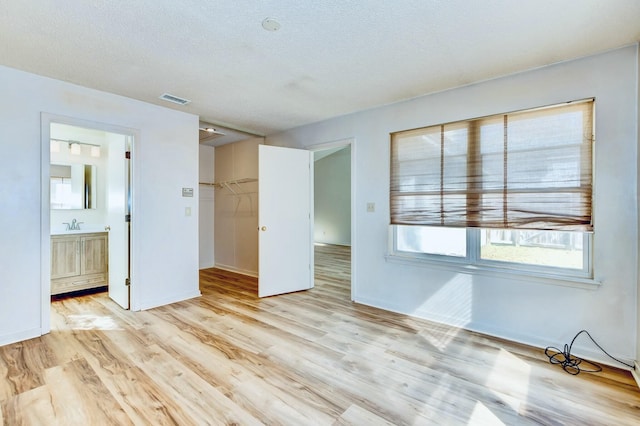 unfurnished bedroom featuring visible vents, baseboards, light wood-style floors, a textured ceiling, and ensuite bath