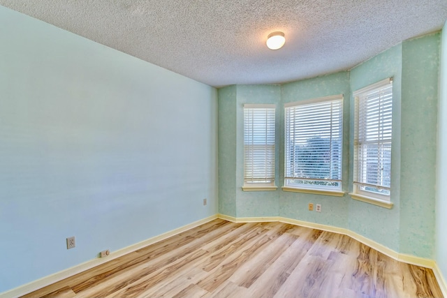 empty room featuring a textured ceiling, baseboards, and wood finished floors