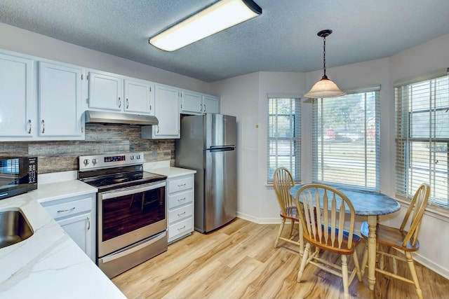 kitchen with light wood-style flooring, under cabinet range hood, appliances with stainless steel finishes, decorative light fixtures, and tasteful backsplash