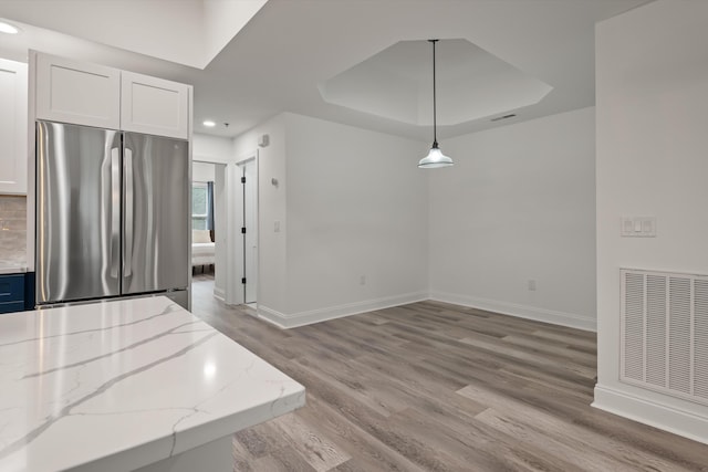 kitchen with stainless steel fridge, hanging light fixtures, light stone countertops, white cabinets, and a raised ceiling