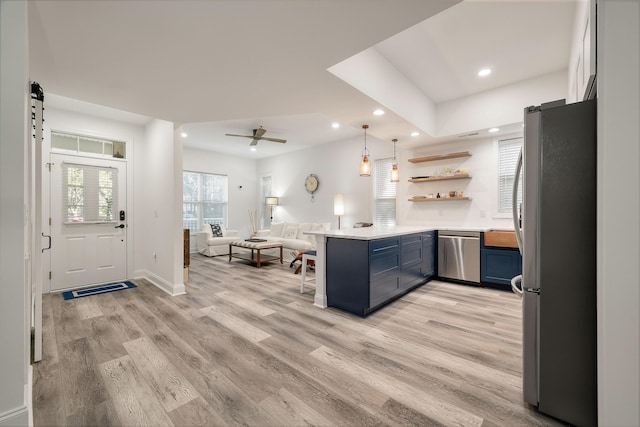 kitchen featuring stainless steel appliances, kitchen peninsula, blue cabinets, a barn door, and light wood-type flooring