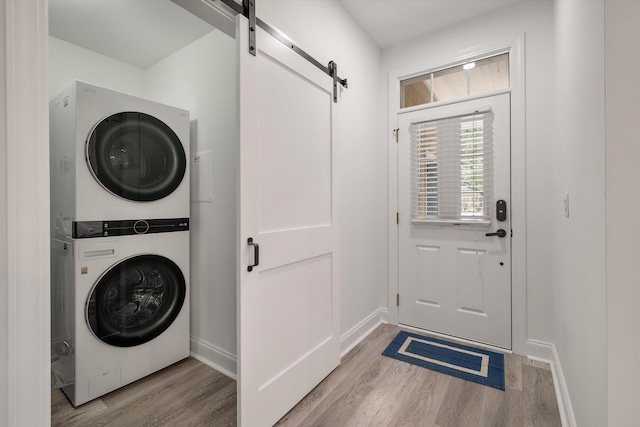 clothes washing area with stacked washer / drying machine, a barn door, and light hardwood / wood-style floors