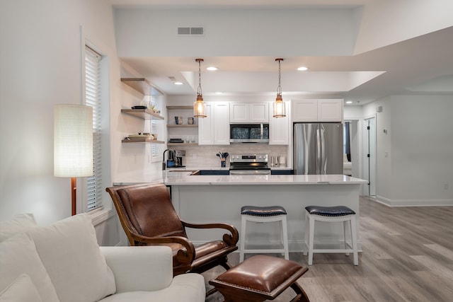 kitchen with a breakfast bar area, tasteful backsplash, appliances with stainless steel finishes, pendant lighting, and white cabinets