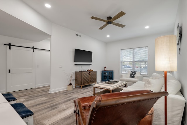 living room with ceiling fan, a barn door, and light hardwood / wood-style floors