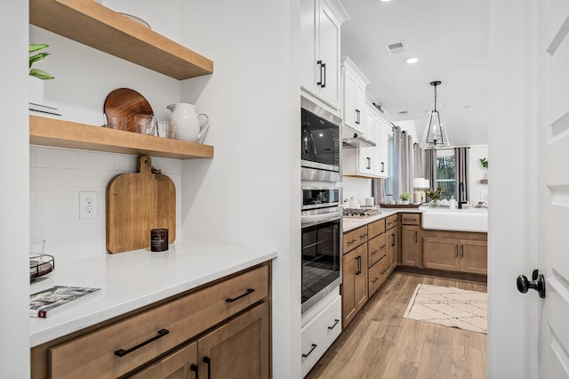 kitchen with visible vents, open shelves, a sink, light wood-style floors, and appliances with stainless steel finishes