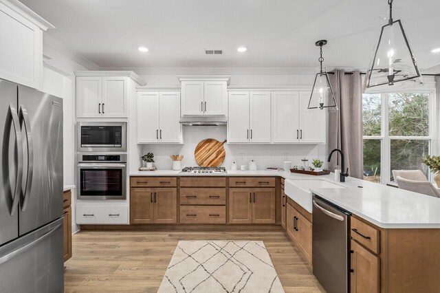 kitchen featuring decorative light fixtures, light wood-type flooring, stainless steel appliances, white cabinetry, and sink