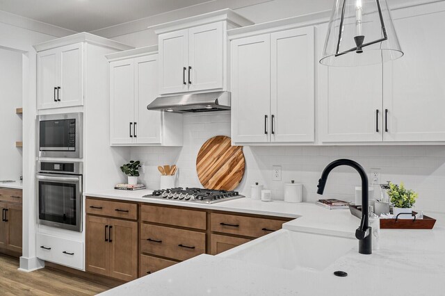 kitchen featuring backsplash, under cabinet range hood, stainless steel appliances, wood finished floors, and white cabinetry