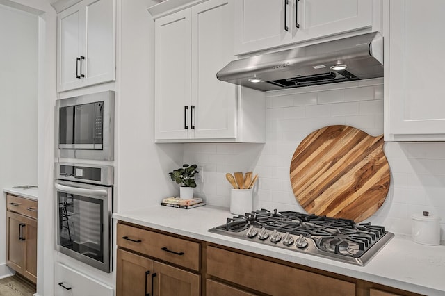 kitchen featuring under cabinet range hood, decorative backsplash, stainless steel appliances, and light countertops