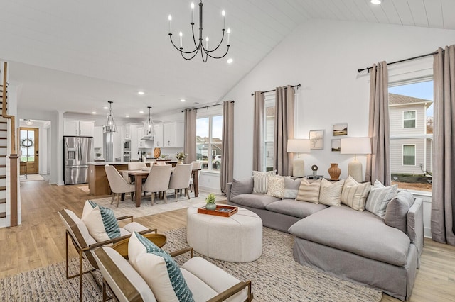 living area featuring a notable chandelier, light wood-style flooring, high vaulted ceiling, and stairs