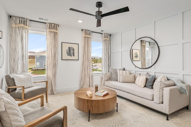 carpeted living area featuring visible vents, a healthy amount of sunlight, a decorative wall, and ceiling fan