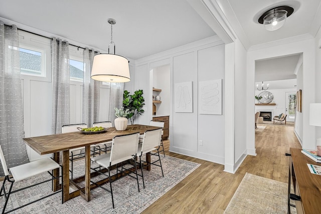 dining area with light wood-style flooring, a fireplace, and ornamental molding