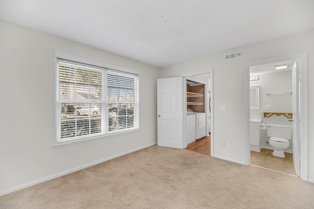 unfurnished bedroom with visible vents, washer and dryer, ensuite bath, carpet, and baseboards