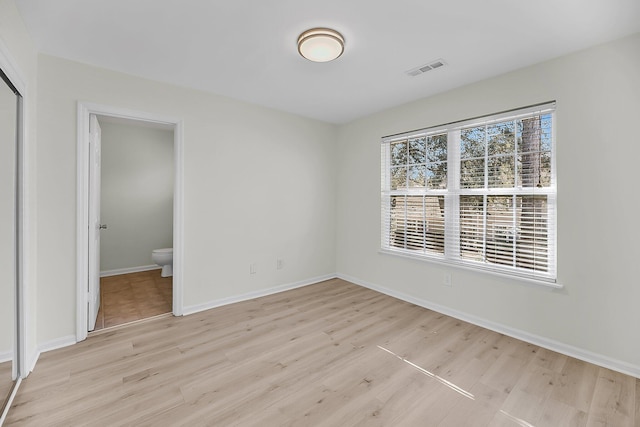 unfurnished bedroom with ensuite bath, visible vents, baseboards, and light wood-style floors