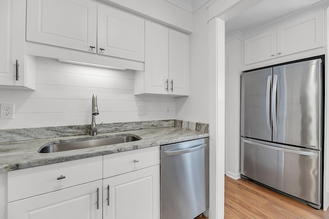 kitchen with light wood-type flooring, a sink, white cabinetry, stainless steel appliances, and light stone countertops