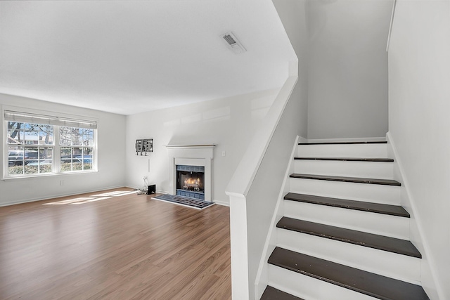 staircase with visible vents, baseboards, a lit fireplace, and wood finished floors