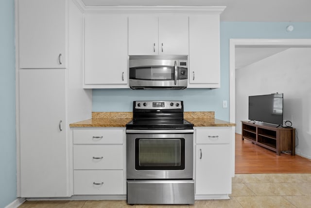 kitchen featuring light tile patterned floors, appliances with stainless steel finishes, white cabinets, and baseboards