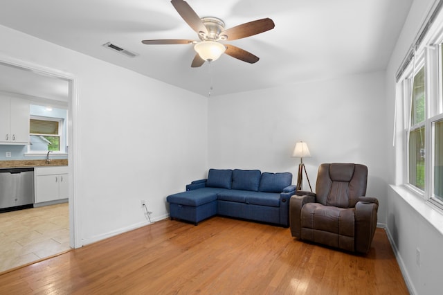 living room featuring a ceiling fan, baseboards, visible vents, and light wood finished floors