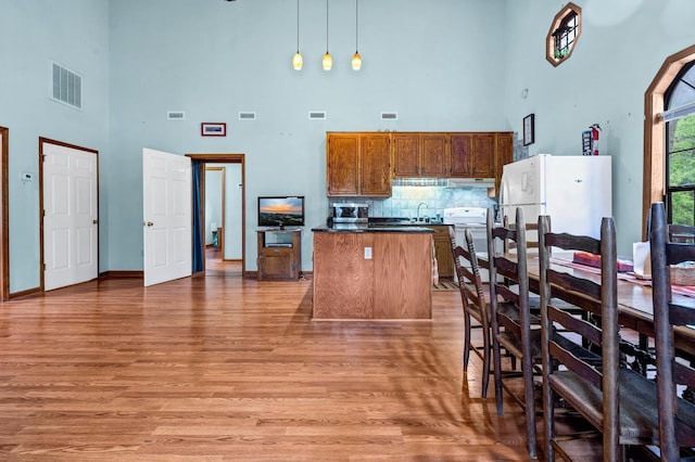 209 Jungle Rd, Edisto Beach, SC 29438 - kitchen with a towering ceiling, white appliances, light wood finished floors, dark countertops, and decorative backsplash