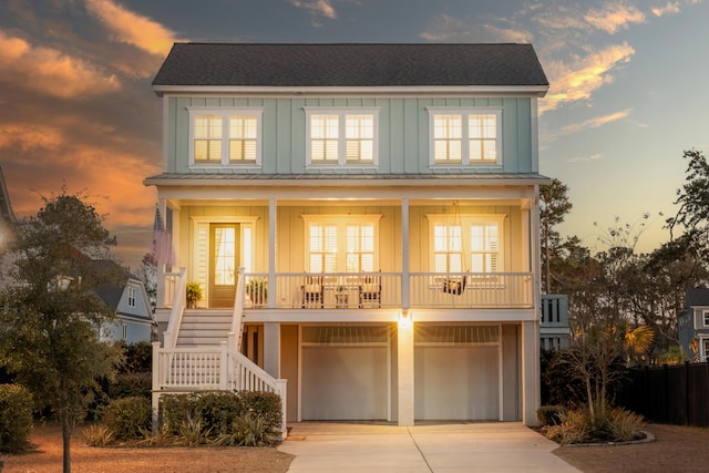 beach home featuring concrete driveway, board and batten siding, covered porch, an attached garage, and stairs