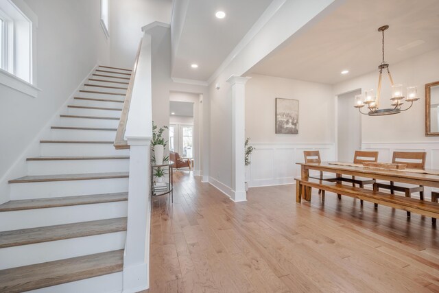 interior space with a wainscoted wall, a decorative wall, light wood-style flooring, stairs, and a notable chandelier