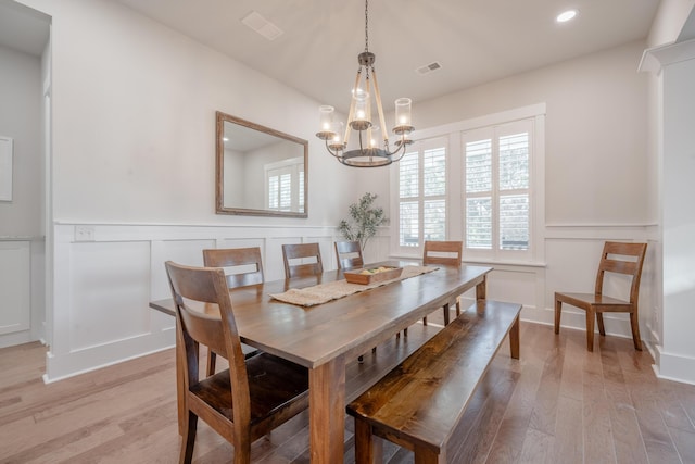 dining area featuring a decorative wall, light wood-style flooring, visible vents, and an inviting chandelier