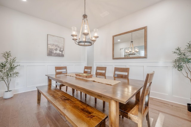 dining room with light wood-type flooring, a decorative wall, a wainscoted wall, and a notable chandelier
