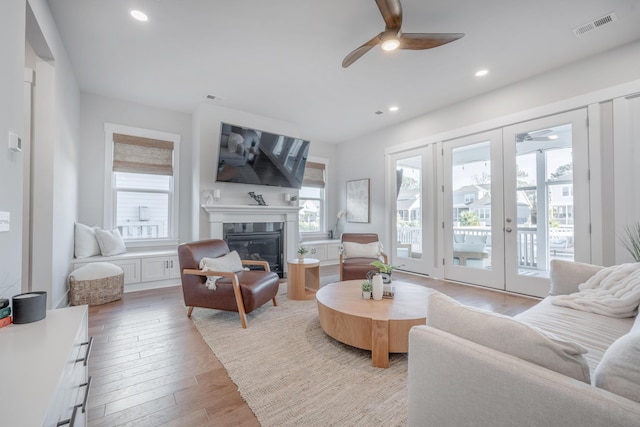 living room with a glass covered fireplace, a ceiling fan, french doors, and visible vents