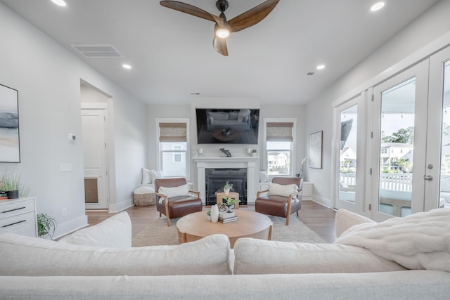 living area with a ceiling fan, a glass covered fireplace, light wood-type flooring, baseboards, and visible vents