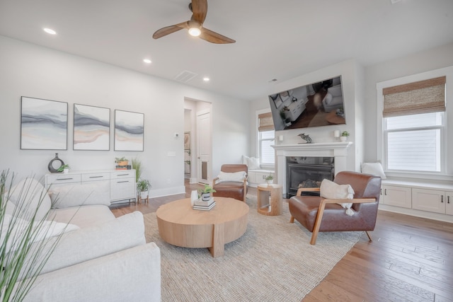 living area with a glass covered fireplace, visible vents, recessed lighting, light wood-style floors, and a ceiling fan
