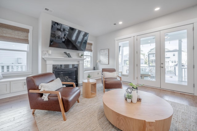 living area featuring recessed lighting, visible vents, french doors, light wood-style floors, and a glass covered fireplace
