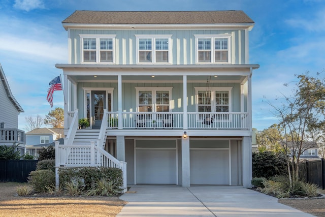 raised beach house featuring driveway, covered porch, a garage, stairs, and board and batten siding