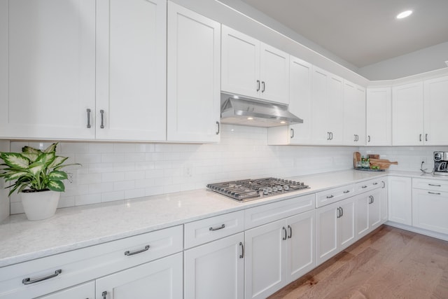kitchen with white cabinets, light wood finished floors, stainless steel gas stovetop, decorative backsplash, and under cabinet range hood