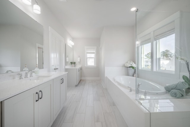 full bathroom featuring two vanities, a garden tub, baseboards, and a sink