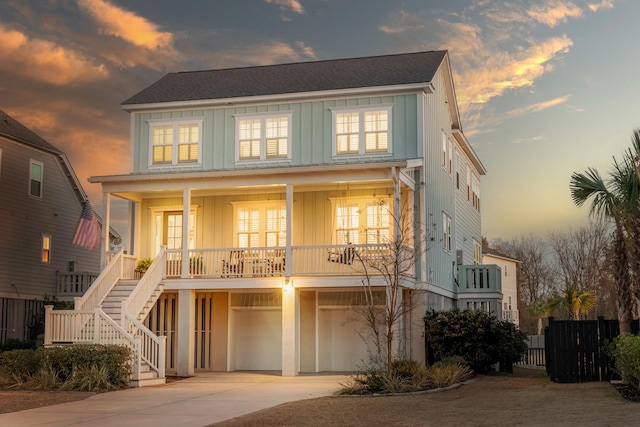 coastal home with driveway, a porch, a garage, stairway, and board and batten siding