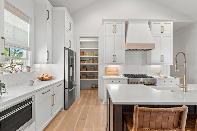 kitchen with premium range hood, lofted ceiling, stove, white cabinets, and high quality fridge