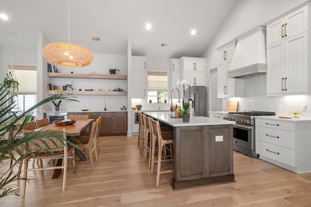 kitchen featuring high quality appliances, open shelves, light wood finished floors, custom exhaust hood, and light countertops