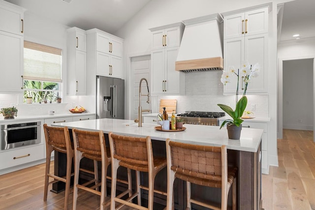 kitchen featuring appliances with stainless steel finishes, light wood-type flooring, light countertops, and premium range hood