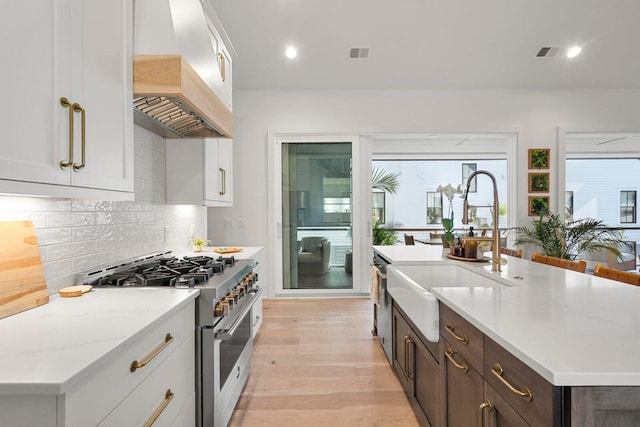 kitchen featuring stainless steel stove, custom exhaust hood, visible vents, and a sink