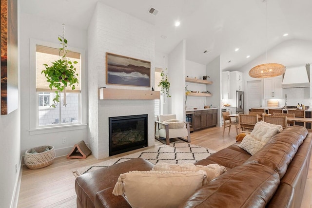 living area with light wood finished floors, visible vents, wine cooler, a fireplace, and high vaulted ceiling