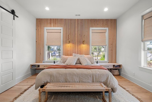 bedroom with a barn door, light wood-style floors, visible vents, and baseboards