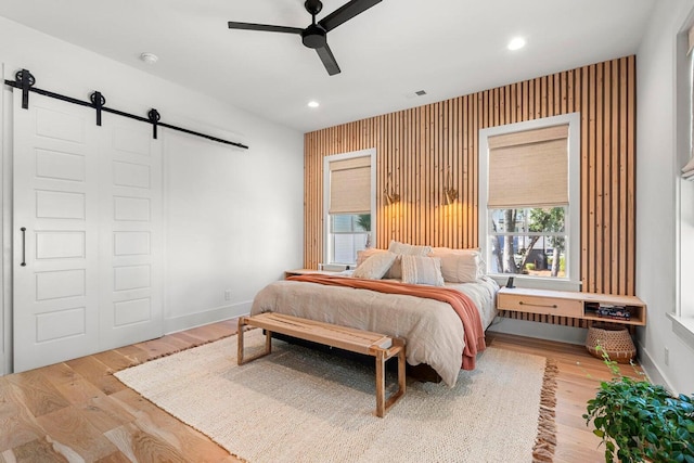 bedroom with a ceiling fan, wood finished floors, baseboards, recessed lighting, and a barn door