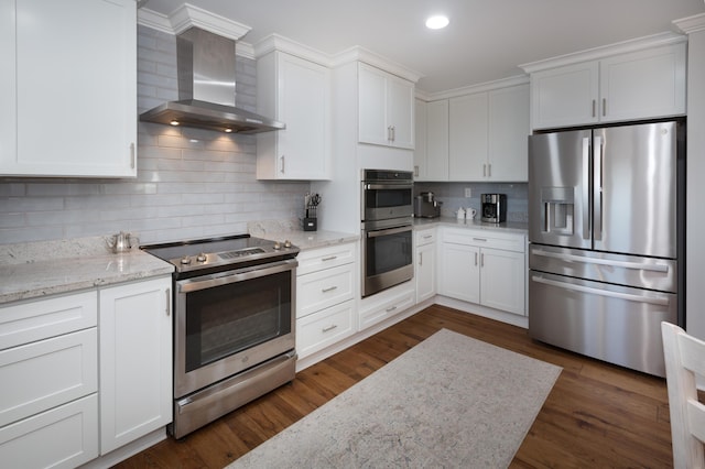 kitchen with decorative backsplash, dark wood-style floors, wall chimney exhaust hood, appliances with stainless steel finishes, and white cabinetry